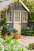 Kleines Gartenhaus mit Blauregen, Funkien in Töpfen