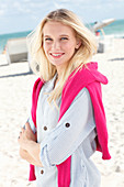 Junge blonde Frau in gestreiftem Hemd und mit pinkfarbenem Pulli am Strand