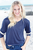 A young blonde woman on a beach wearing a long-sleeved blue shirt