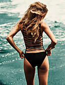 A young blonde woman on a beach wearing a black bathing suit