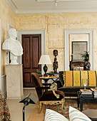 Brown velvet armchair in living room with large plaster bust on plinth and African Mende carvings