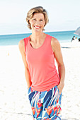 A mature woman on a beach wearing a salmon-coloured top and colourful trousers