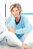 A mature woman wearing a blue jumper and white trousers