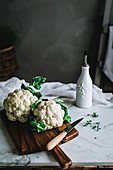 Cauliflower with green leaves lying on wooden cutting board
