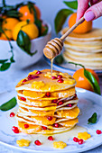 Pancake with Mandarin oranges, pomegranate seeds and maple syrup pouring from a spoon