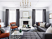 Gray upholstered furniture, coffee table and cognac-colored leather chairs in front of a fireplace in an elegant living room with a light gray wall