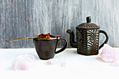 Rosenblütentee in schwarzer Keramiktasse und Teekanne
