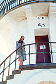 A young brunette woman wearing a coat and a scarf in a lighthouse