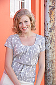 A blonde woman wearing a grey spotted blouse and a white skirt