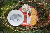Plate with bear motif and biscuits in nest of conifer branches and fairy lights