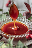 Rose hip jam dripping from a spoon into a glass bowl
