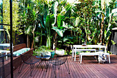 Wooden terrace with outdoor furniture, surrounded by tropical plants