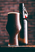 A glass of dark beer with an open bottle of beer in the background