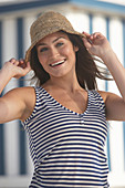 Junge brünette Frau mit blauweiß gestreiftem Top und Sommerhut am Strand