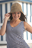 A young brunette woman on a beach wearing a blue-and-white striped top and a summer hat