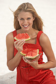 Junge blonde Frau im roten Sommerkleid hält ein Stück Wassermelone