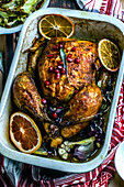 Baked chicken in ceramic form decorated with orange slices, pomegranate seeds and sage leaves