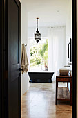 Waschtisch aus Holz und frei stehende Badewanne vor Fenster mit Gartenblick