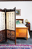 Screen with Chinese characters in front of a vintage wooden double bed