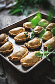 Baking tray with composed freshly baked pies having golden crispy crust and garnishes with green