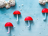 Babybel cheese umbrellas on light blue paper with striped straws as base with white cauliflower clouds and rain drops