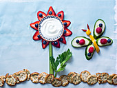 Creative flower and butterfly made of fruits and vegetables with berry petals, yogurt center and celery stalk