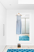Summer dress on wall mirror, blue carpet and wardrobe in white bedroom