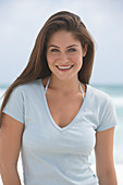 A young brunette woman on a beach wearing a beige top