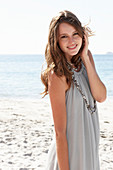 A young brunette woman on a beach wearing a beige summer dress and a necklace