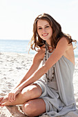 A young brunette woman on a beach wearing a beige summer dress and a necklace