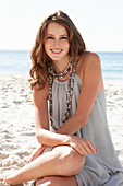 A young brunette woman on a beach wearing a beige summer dress and a necklace