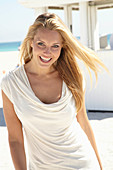Blonde Frau in beigem Sommerkleid am Strand