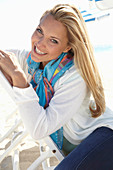 Blonde Frau mit buntem Halstuch und weißer Jacke am Strand