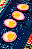 Eggs pickled in beetroot, halved, on a blue ceramic plate