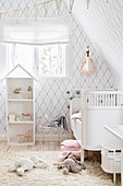DIY-Puppenhaus und weißes Babybett in hellem Zimmer mit Rauten-Tapete