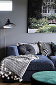 Blue sofa combination with scatter cushions and blanket, standard lamp and picture on grey living-room wall