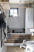 Mit rustikalen Brettern verkleidete Badewanne vor grauer Wand