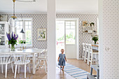 Little girl walking along runner between dining area with white furniture and kitchen