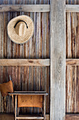 Folding chair below straw hat hung on rustic wooden wall