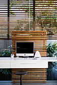 Computer on whit desk against glass wall with louvre blinds