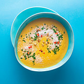 Carrot soup with coconut and chili in a blue bowl on a blue background