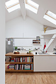 Island counter running into shelves in white kitchen with skylights