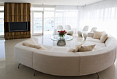 Weißes Designersofa vor Fenster und Fernsehregal mit Holzverkleidung in offenem Wohraum