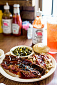 Side angle of barbecue pork ribs and pulled pork covered in sauce with collard greens and cornbread muffin
