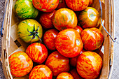 Beautiful, homegrown tomatoes with red, yellow, and green fresh skins in woven baskets on burlap tablecloth