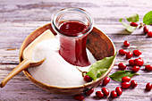 A bottle of homemade cornelian cherry syrup in a wooden bowl with sugar