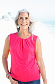 Reife Frau mit weißen Haaren in rosa Top und Bluejeans am Strand