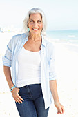 A mature woman with white hair on a beach wearing a striped blouse, a top and blue jeans