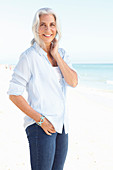 A mature woman with white hair on a beach wearing a striped blouse, a top and blue jeans