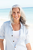 Reife Frau mit weißen Haaren in gestreifter Bluse und Top am Strand